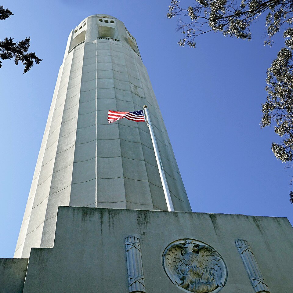 The fluted shaft of Coit Tower and the carved seal over its entrance, the flag flying above