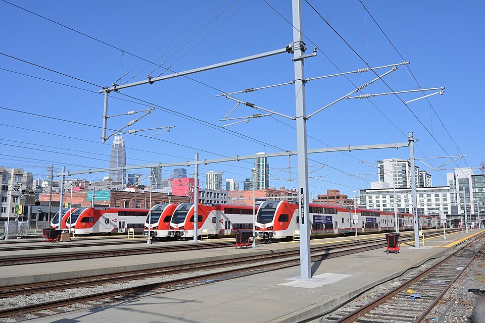 Red-and-white electric Caltrain trains at Fourth and King, downtown towers behind