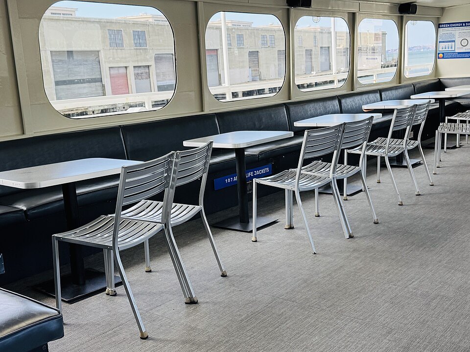 Tables and chairs in the cabin of an Alcatraz ferry, the pier sheds through its windows
