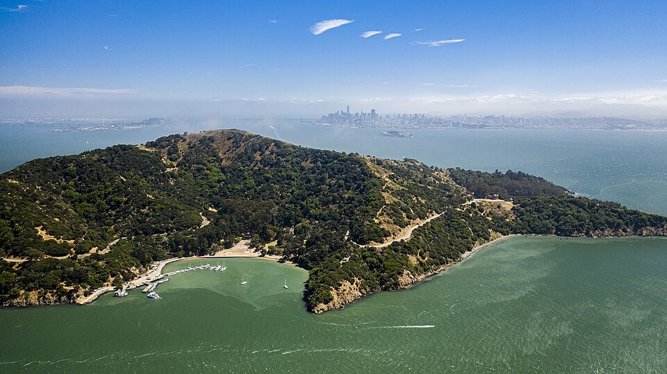 Angel Island from the air, its wooded ridge and beaches in the bay, the city in the distance
