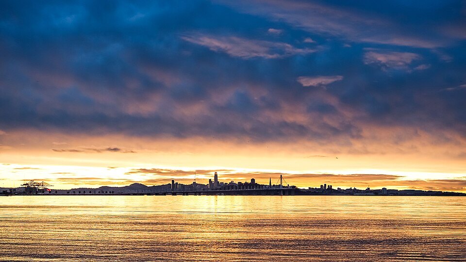 The city's skyline silhouetted across the bay under a blazing sunset