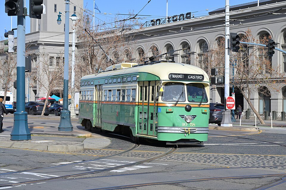 A green heritage streetcar turning in front of the Ferry Building's arcade