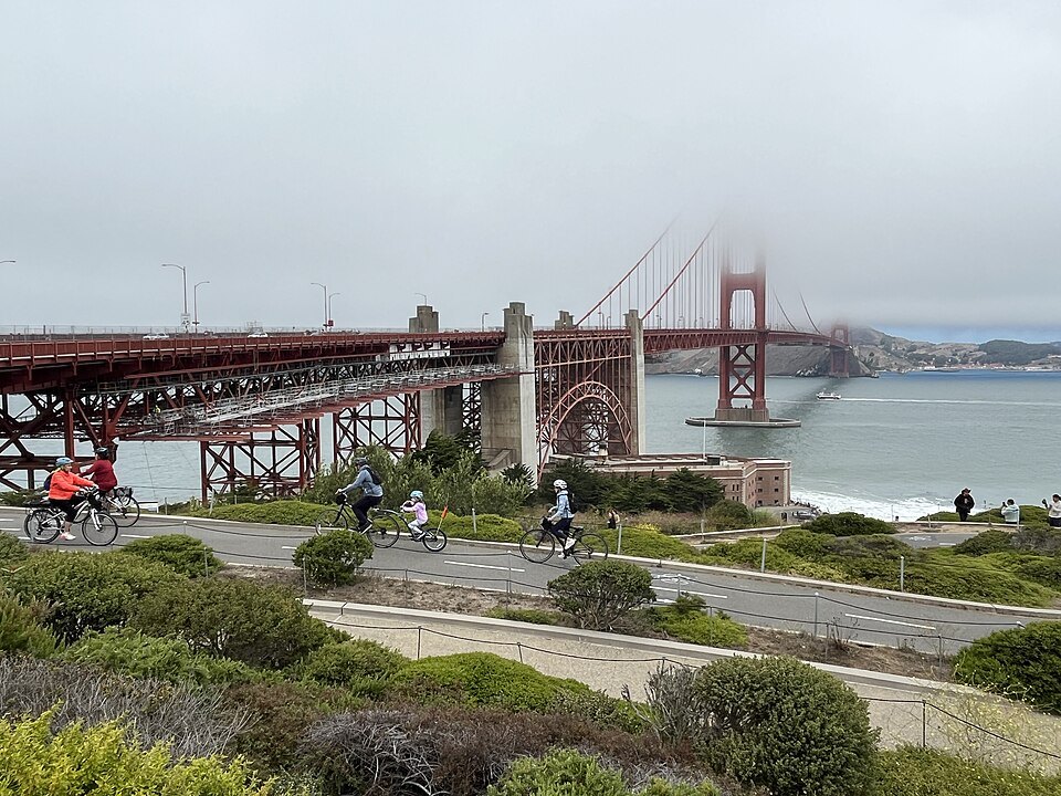 Cyclists on the path toward the bridge's south end, its towers in thin fog