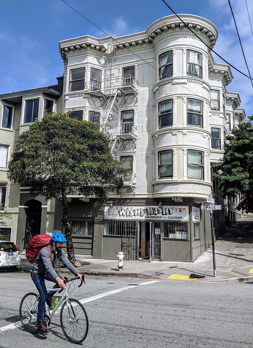 A white bay-windowed apartment house on a Haight corner, a cyclist passing