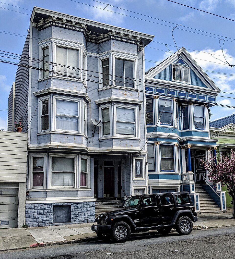 Tall gray bay-windowed Victorians side by side on a sloping street