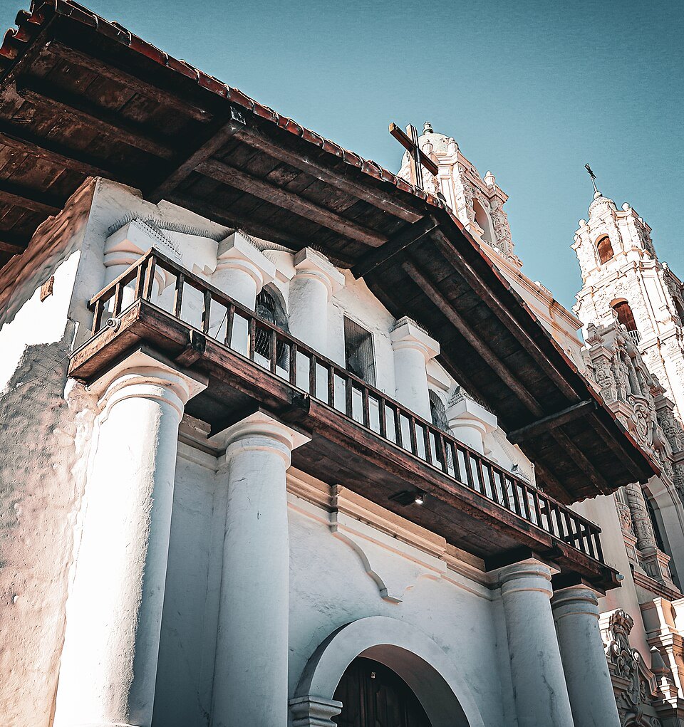 The carved front and balcony of the old Mission Dolores chapel, the basilica tower beside it