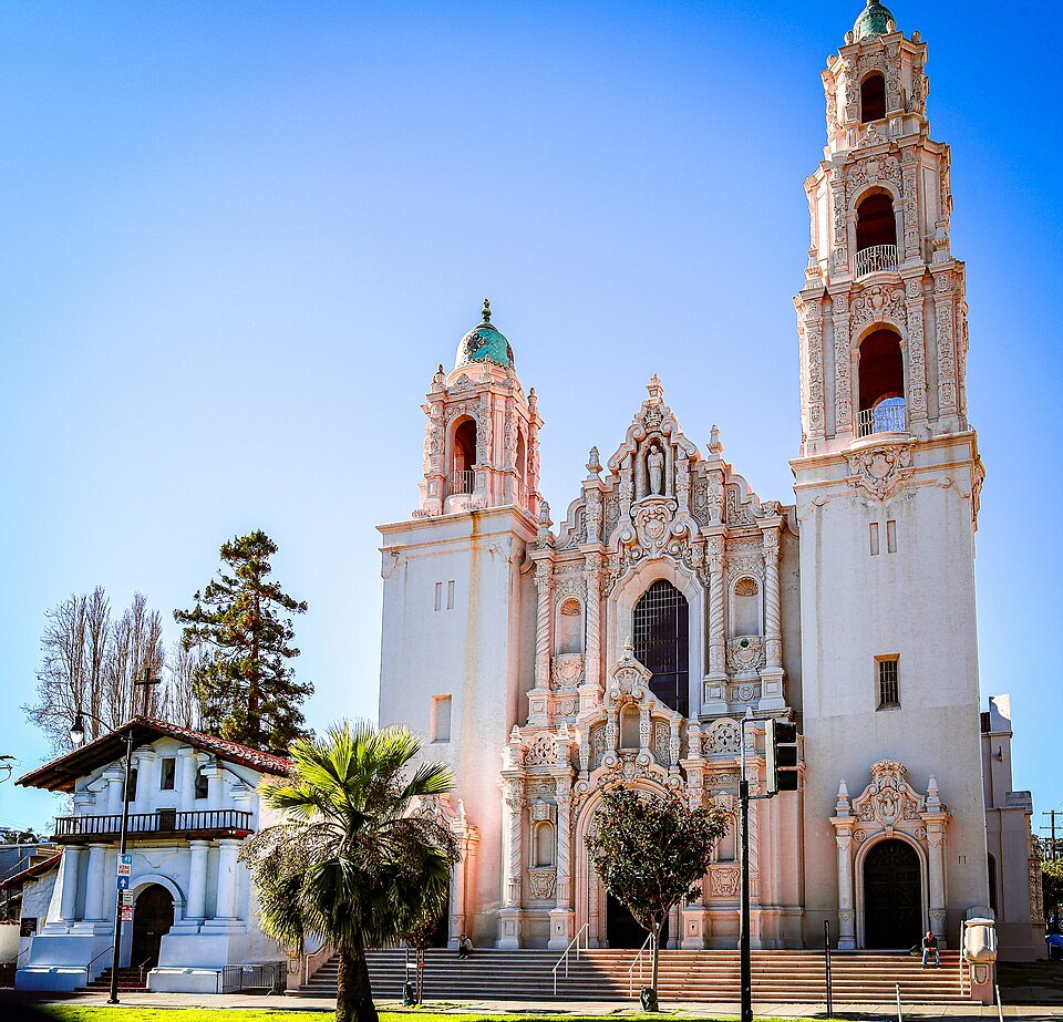 The small white adobe chapel of Mission Dolores beside the towers of the basilica
