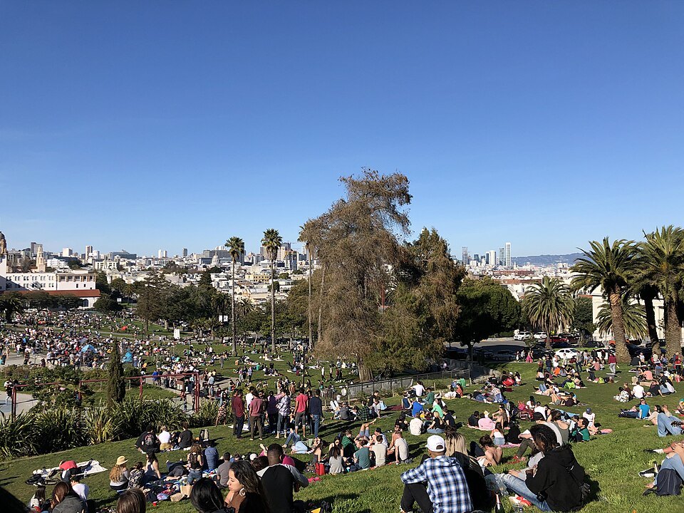 Mission Dolores Park full on a warm day, palms and houses behind