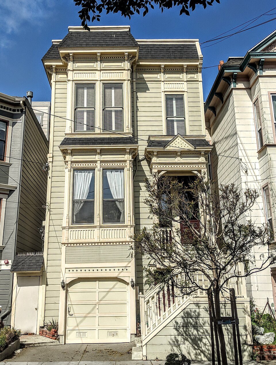 A narrow cream Victorian with a garage under its bay windows