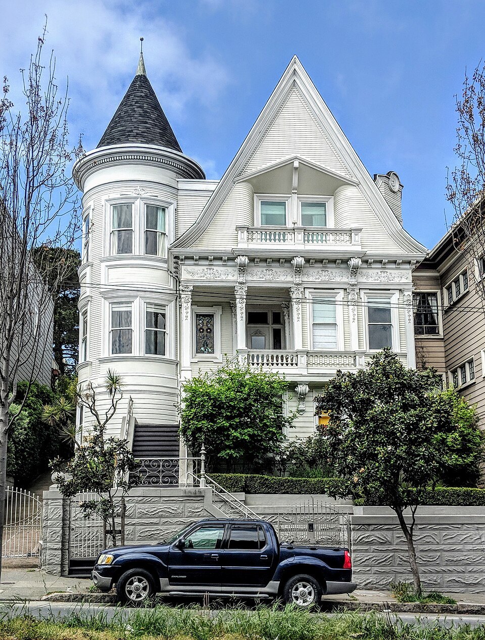 A white Victorian with a pointed turret, up a flight of steps from the street