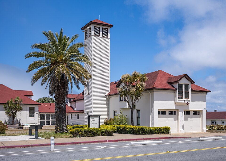 A white chapel tower and red-roofed buildings among palms in the Presidio