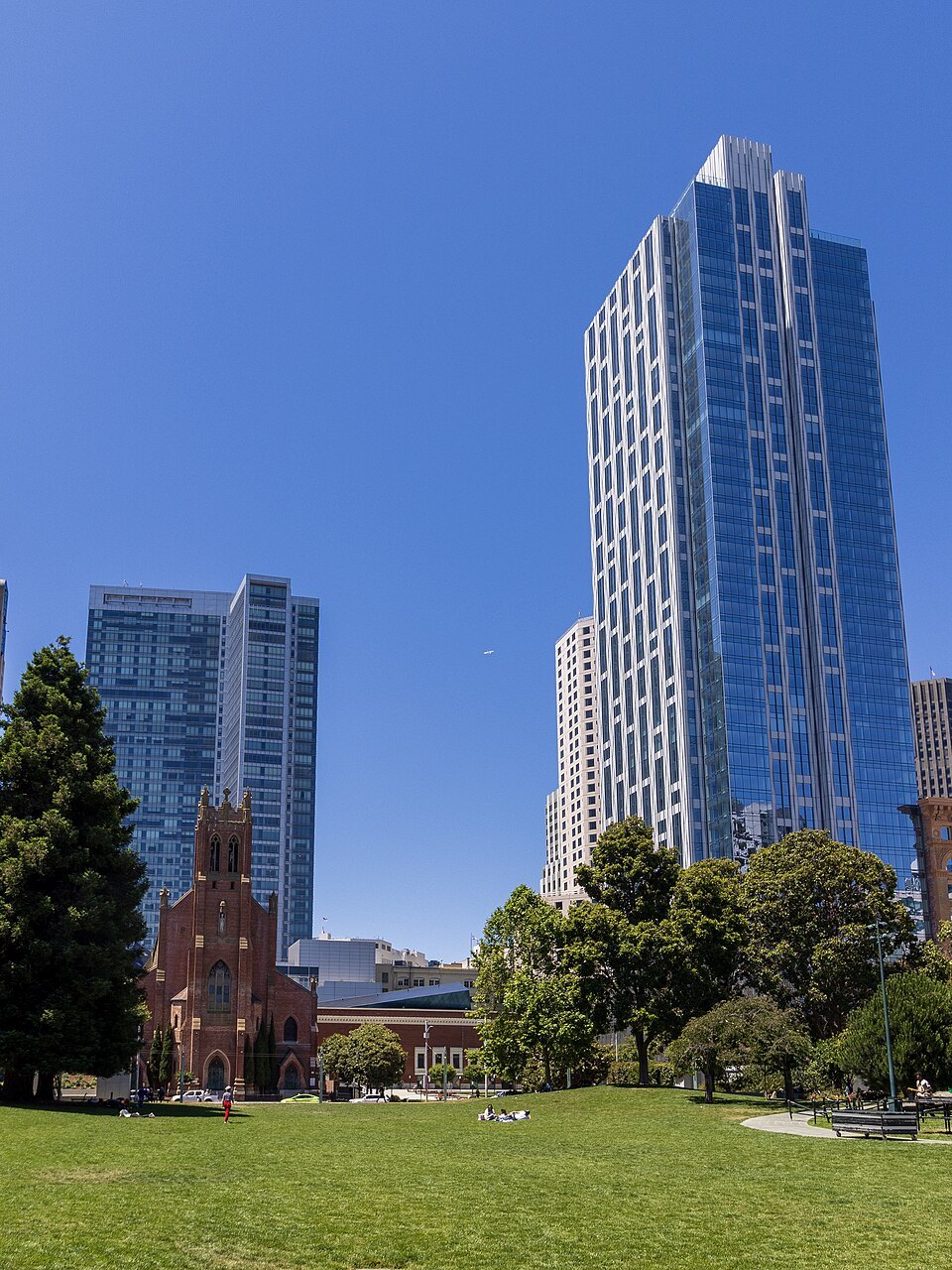 Glass towers rising beyond the trees of Yerba Buena Gardens, a brick church at their foot