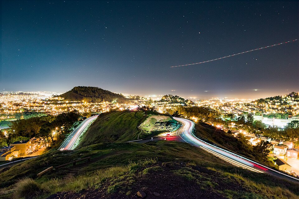 Car lights tracing the road around Twin Peaks at night, the city lit below